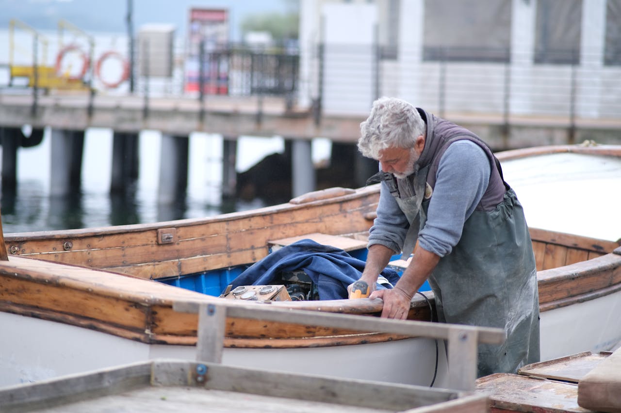 Elderly fisherman working on a wooden boat by the dock in Türkiye, a tranquil outdoor scene.